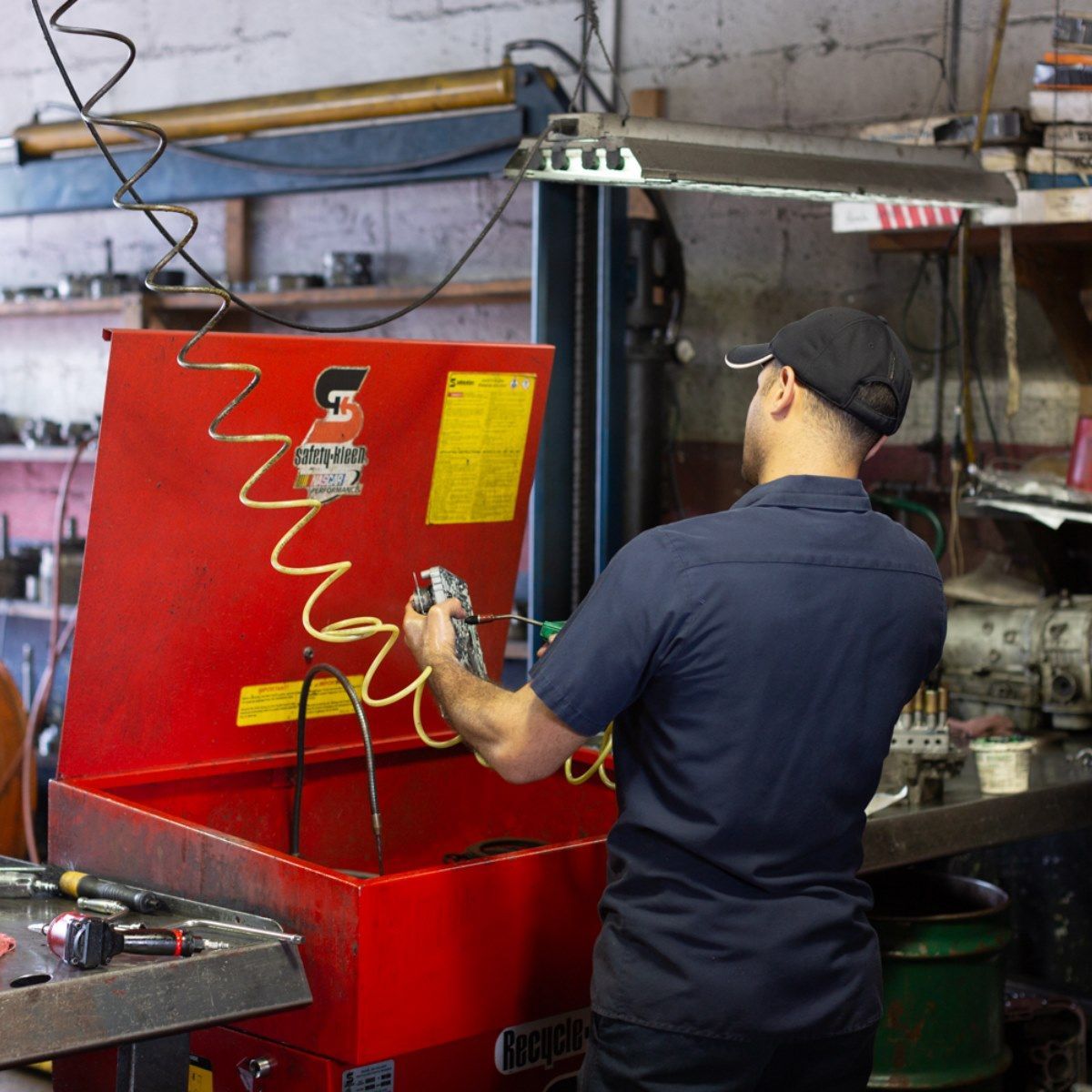 Worker operating a red industrial machine in a workshop, with a coiled hose overhead