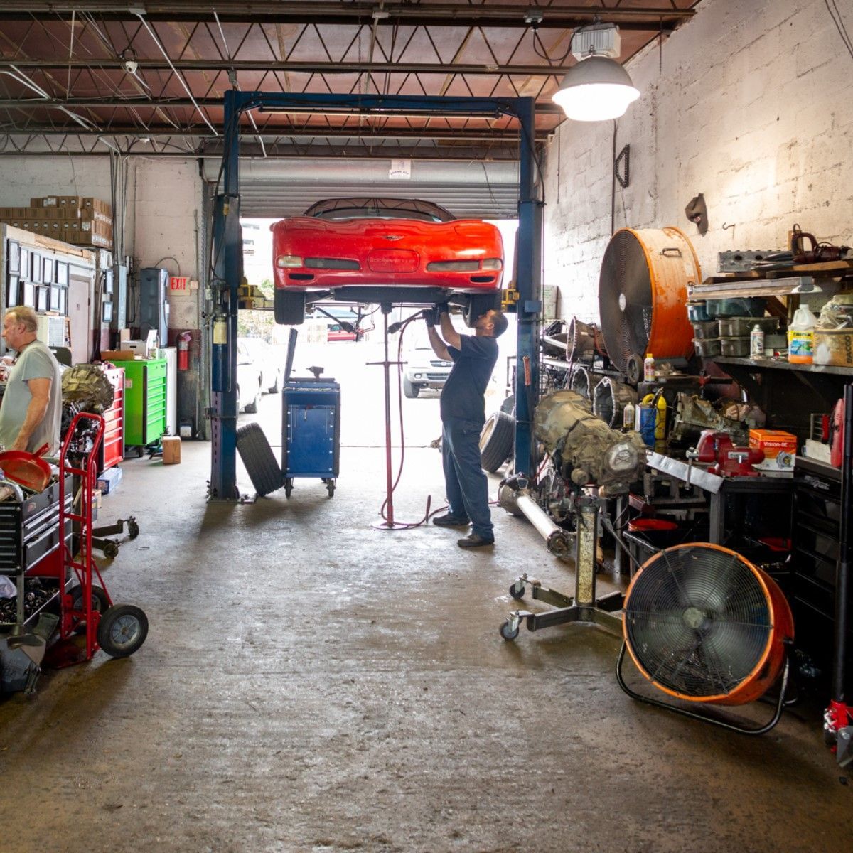 Auto repair shop with a red car lifted on a hoist and a mechanic working underneath