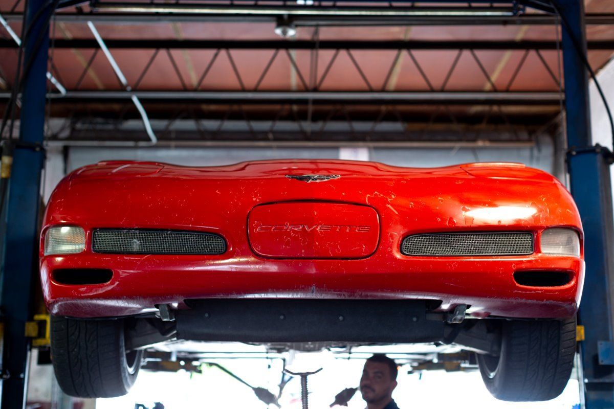 Red sports car lifted on a hoist in a garage, viewed from the front.