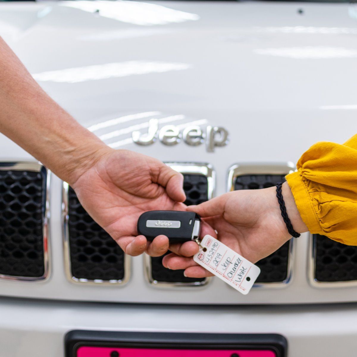 Hands exchanging a Jeep key fob in front of a white Jeep grille and logo.