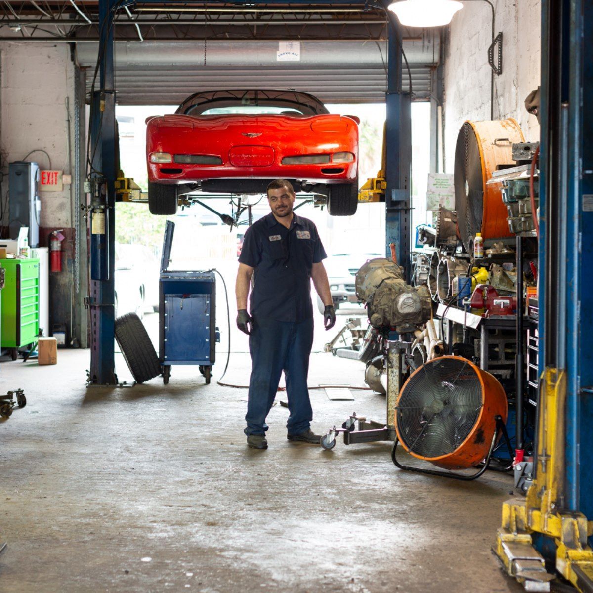 Auto mechanic standing in a garage beneath a red car on a lift