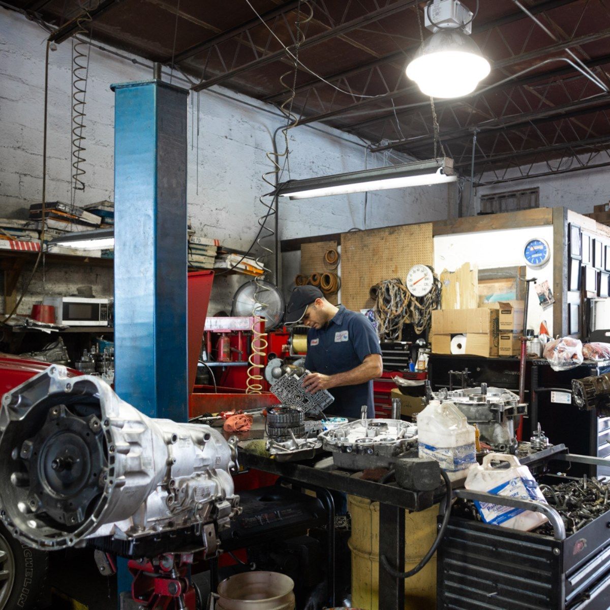 Mechanic working in a cluttered auto repair shop beside a car engine and tools