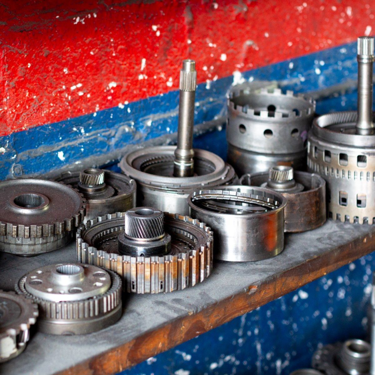 Assorted metal gears and machine parts on a shelf against a red and blue wall