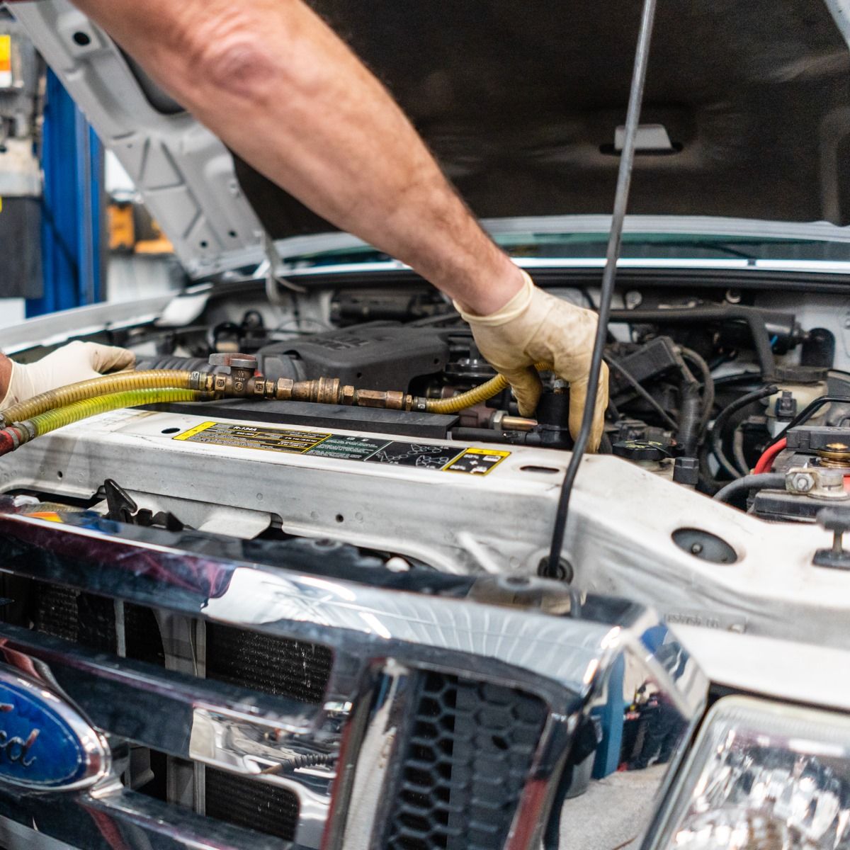 Mechanic working on a vehicle engine under the open hood in a repair shop