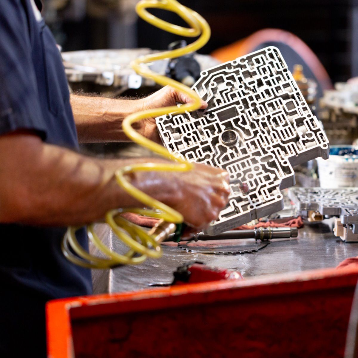 Hands holding a yellow coiled hose over a red workbench with a metal cutout piece in a workshop