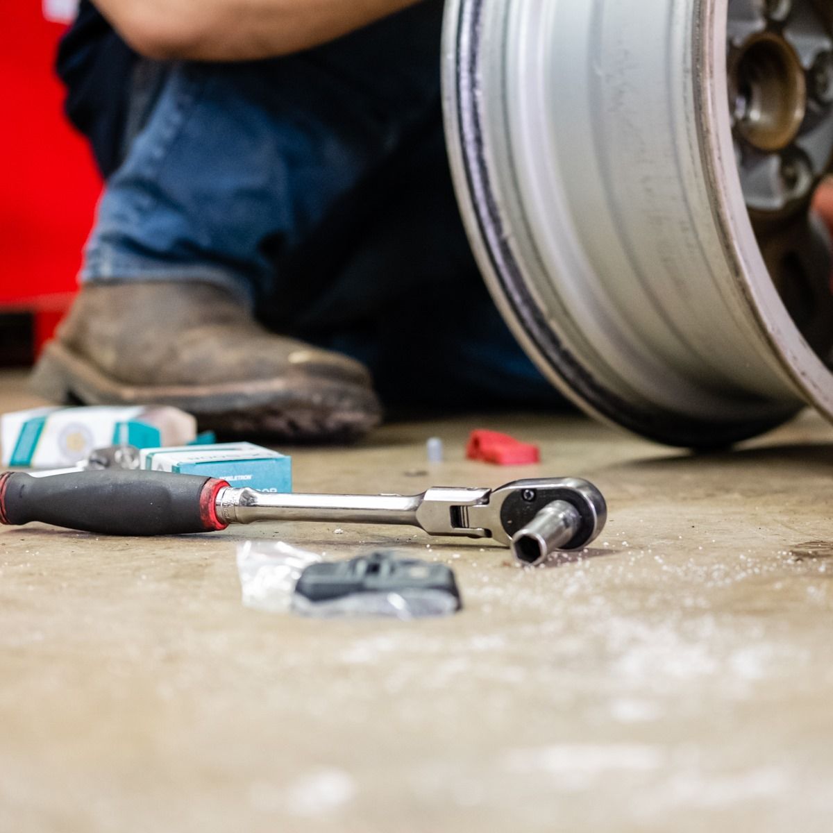Mechanic’s tools on the floor beside a car wheel and a crouched worker in a workshop