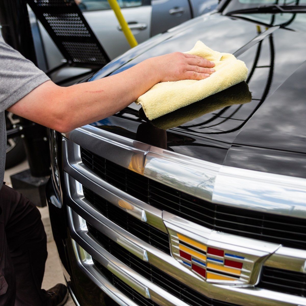 Person wiping the hood of a black Cadillac SUV with a yellow cloth