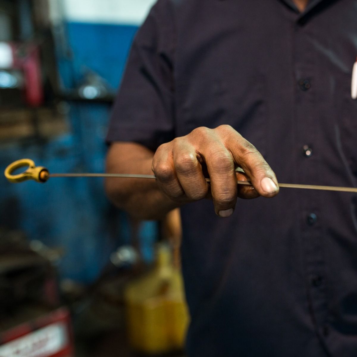 Hand holding a metal dipstick or rod in a workshop, with a blurred blue background