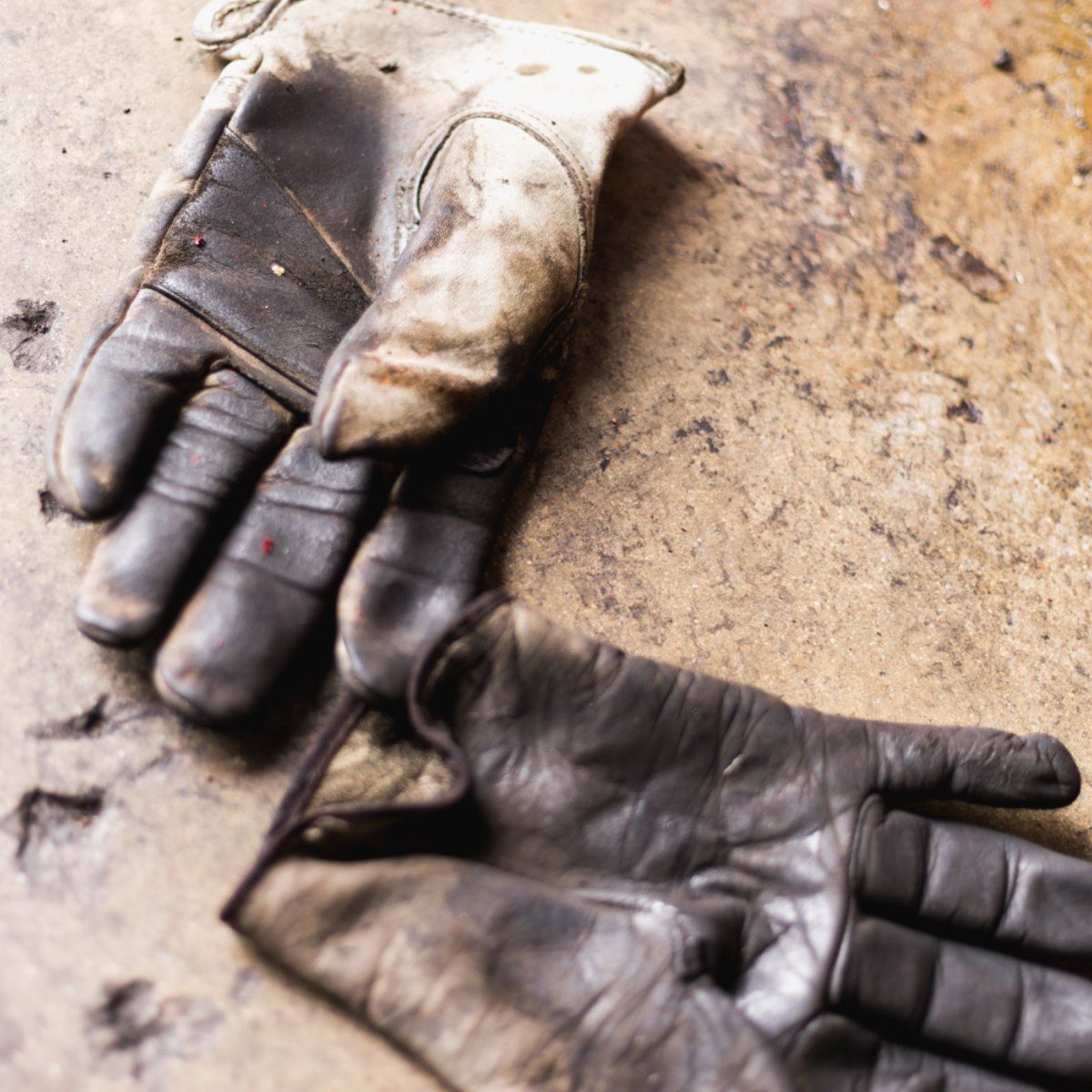 Two dirty work gloves lying open on a dusty ground, one black and one beige.