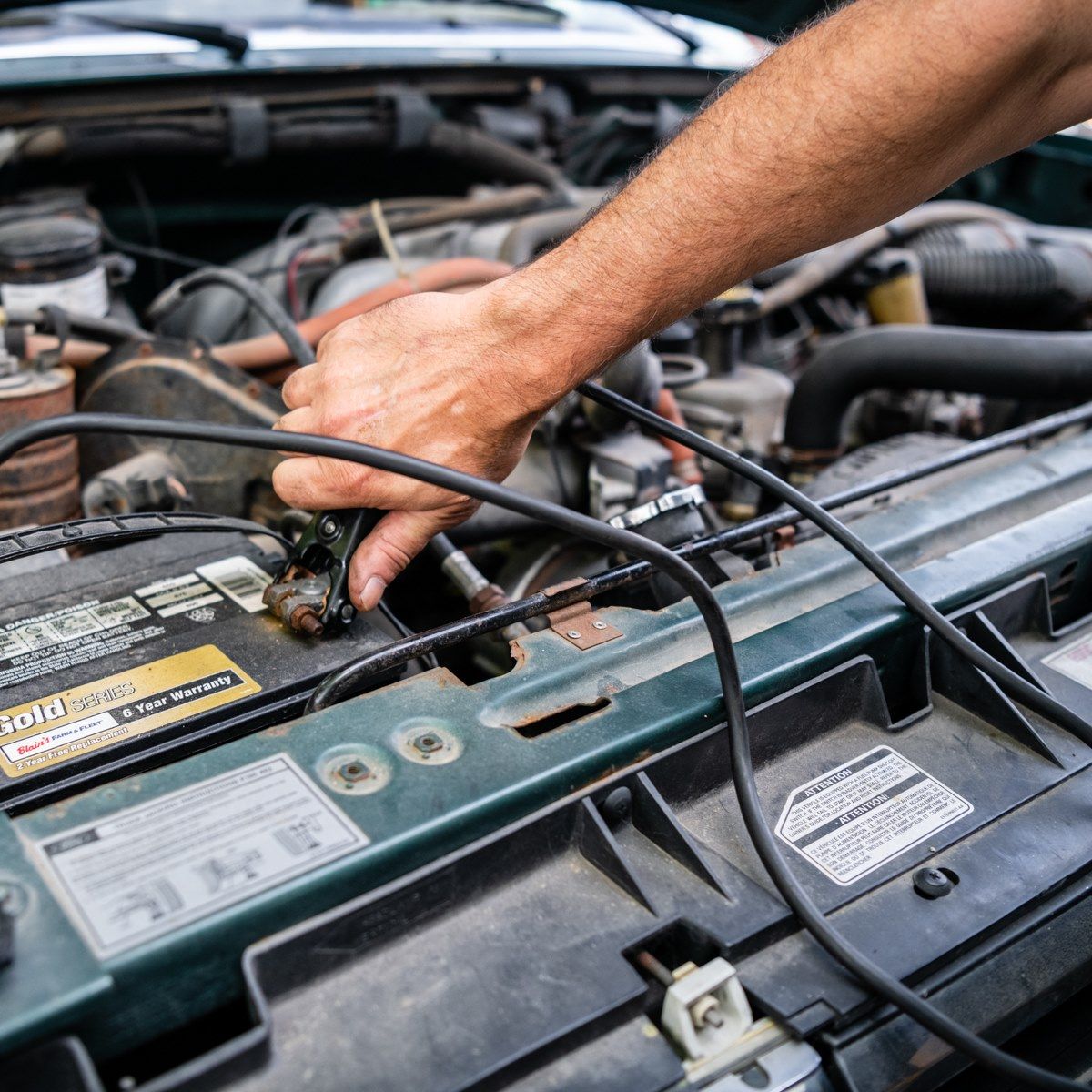 Hand reaching into a car engine bay, checking components and wires