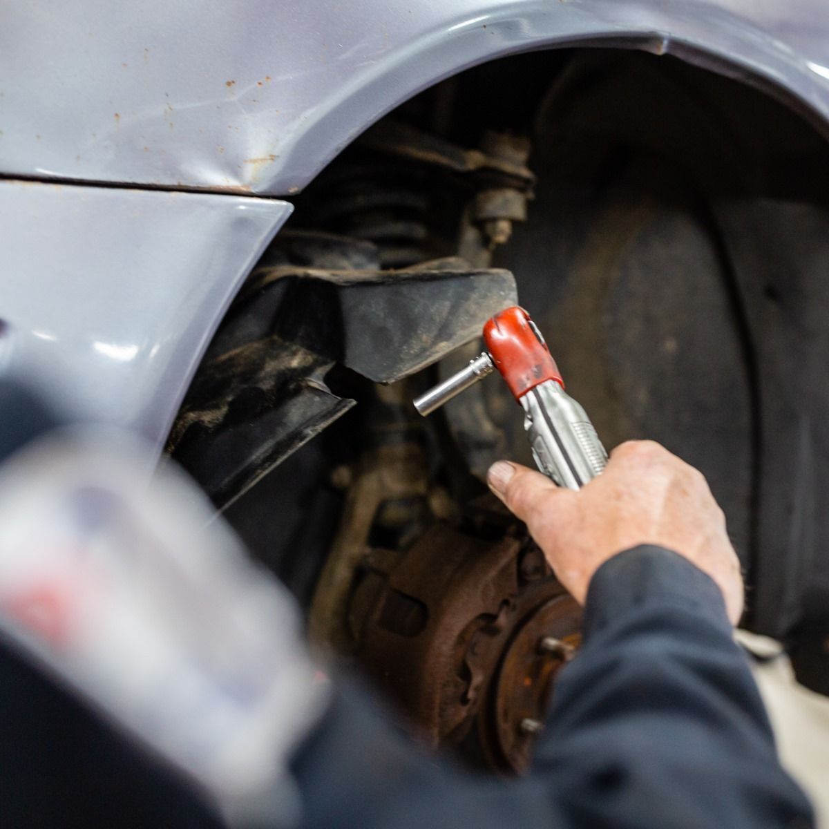 Mechanic using a red tool on a car’s front wheel well during repair