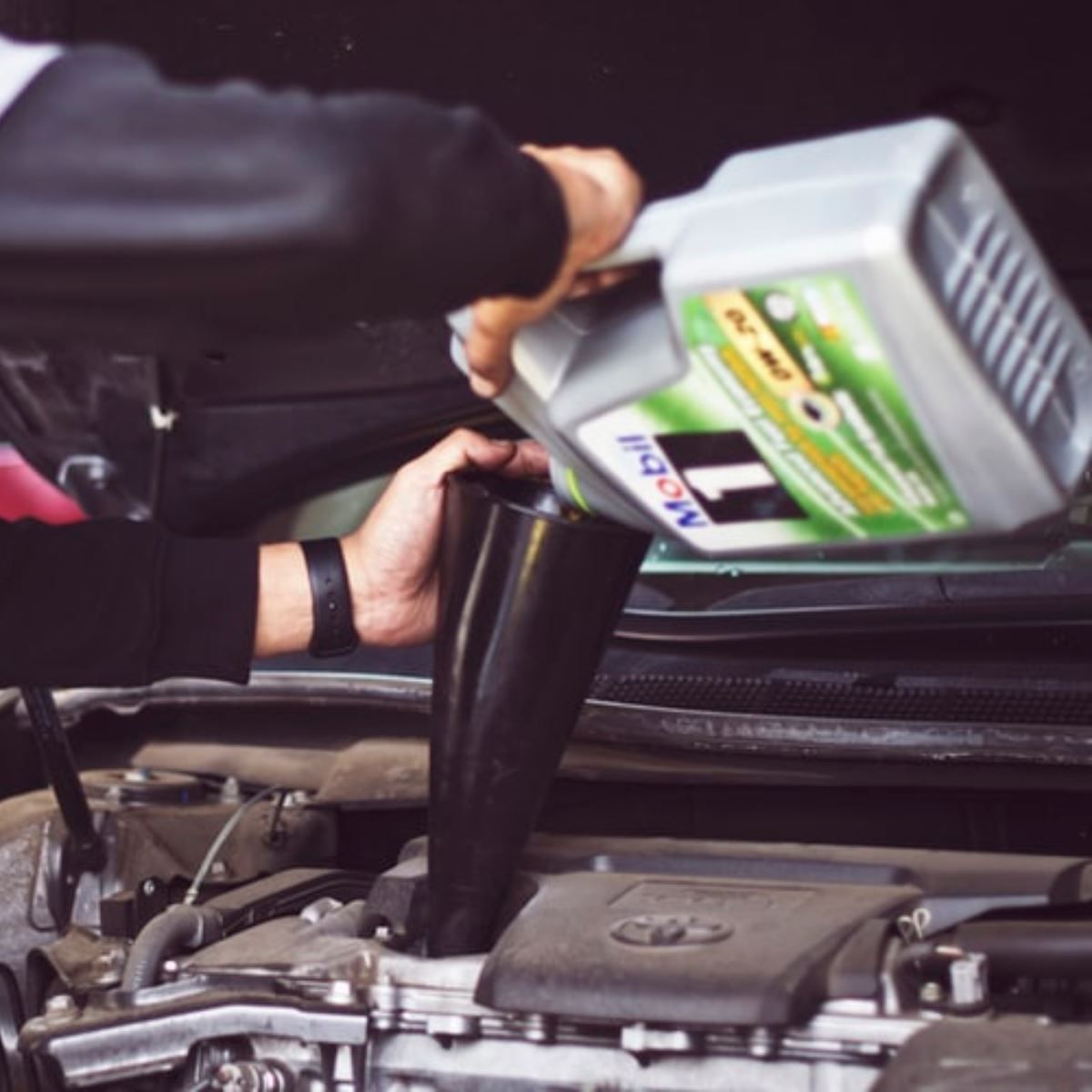 Pouring motor oil into a car engine through the hood opening
