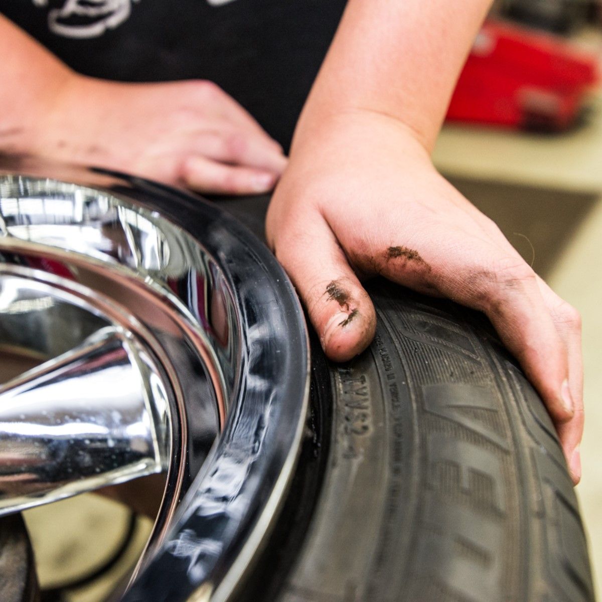 Hand inspecting a car tire beside a chrome wheel, with grease on the fingers