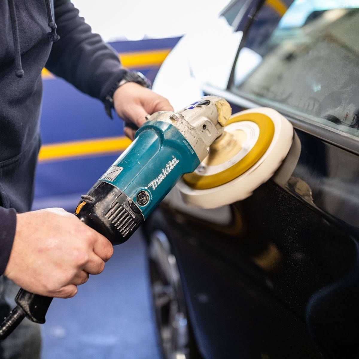Person polishing a black car with a buffer in an auto shop