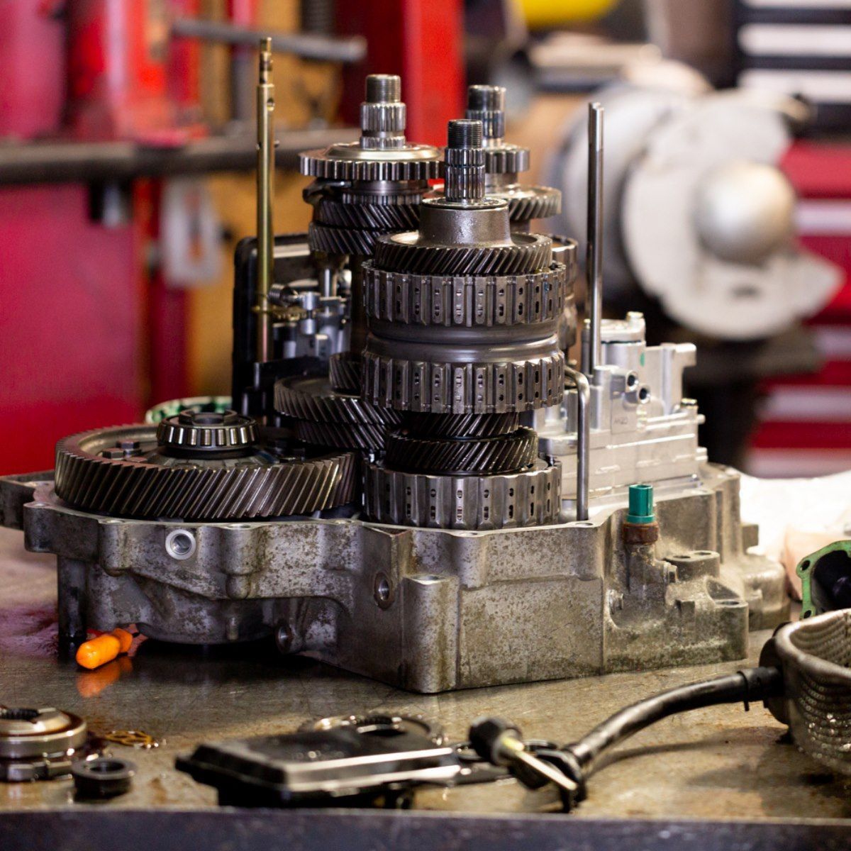Close-up of metal gears and machine parts on a workshop bench, with tools blurred in the background