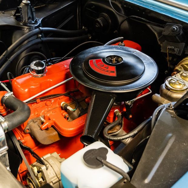 Classic car engine bay with bright orange engine, black air cleaner, and chrome components