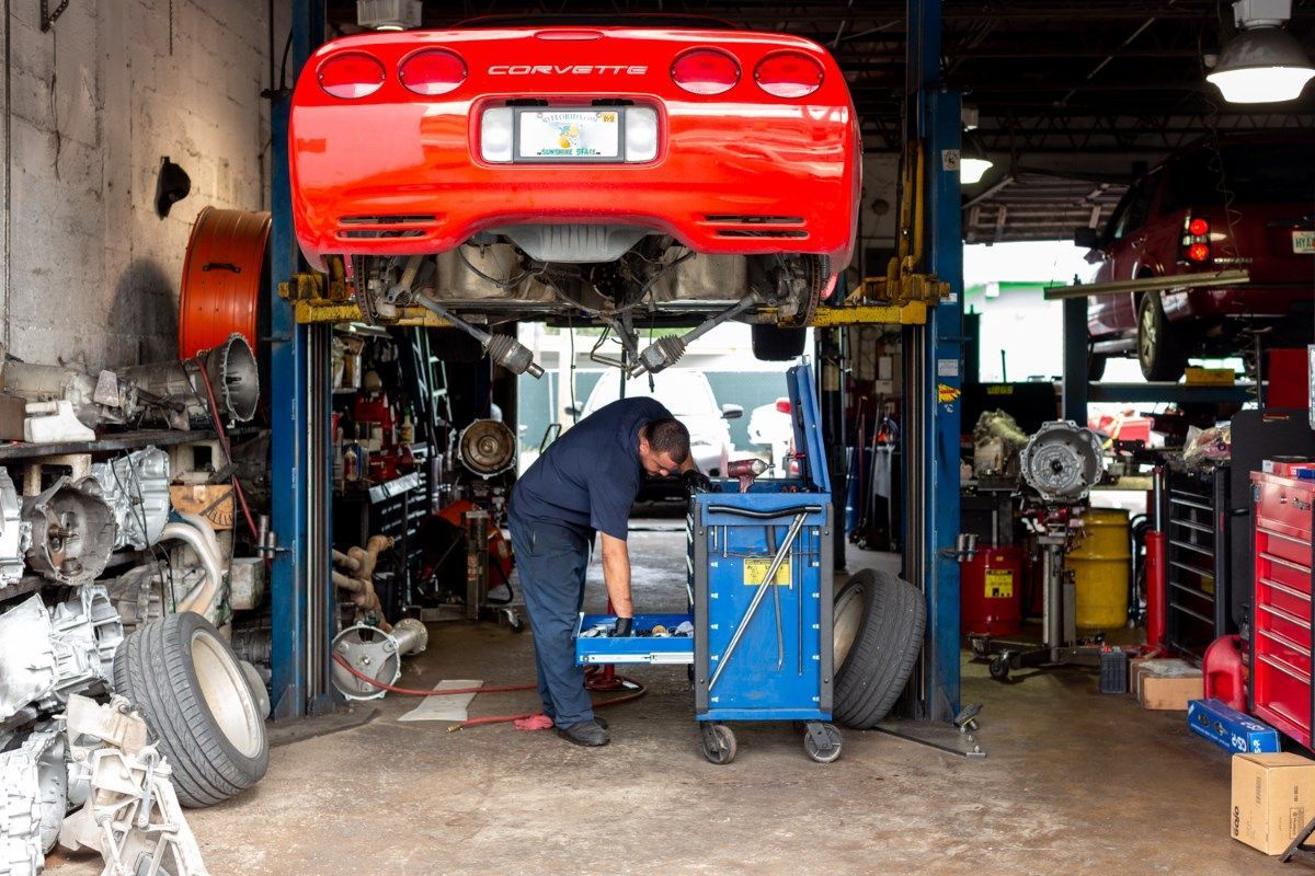 Mechanic working under a red sports car on a lift in a cluttered auto repair garage