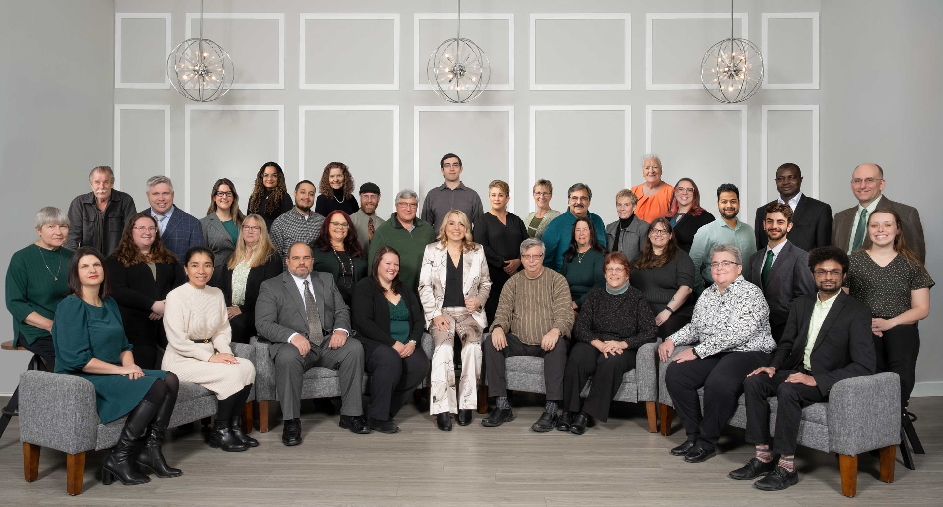 Group of people, mostly in business attire, posing together in a studio setting with a gray backdrop.