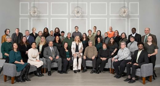 Group of people, mostly in business attire, posing together in a studio setting with a gray backdrop.