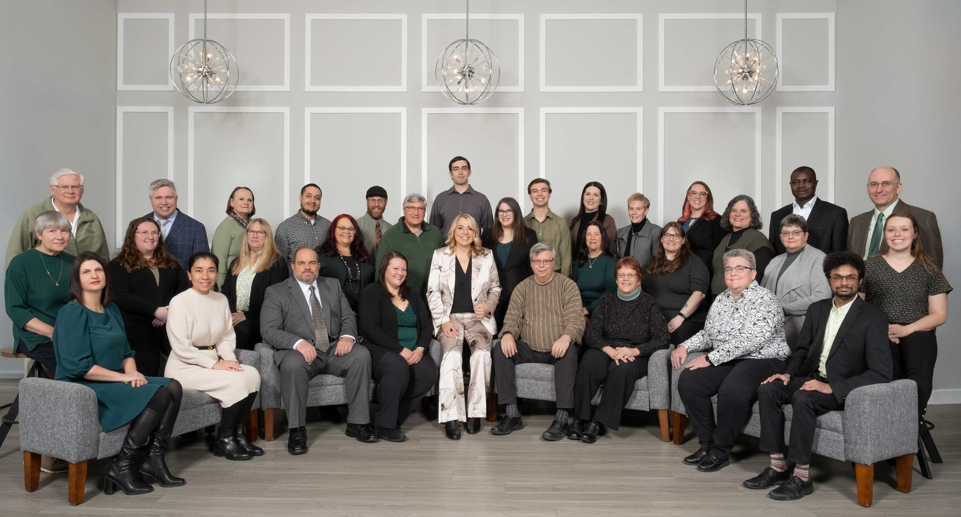 Group of people, mostly in business attire, posing together in a studio setting with a gray backdrop.
