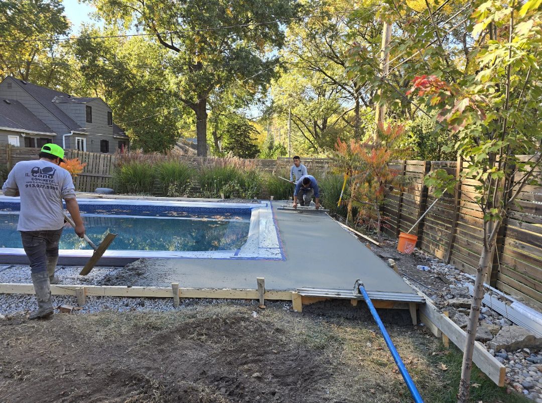 A man is working on a concrete deck next to a swimming pool.