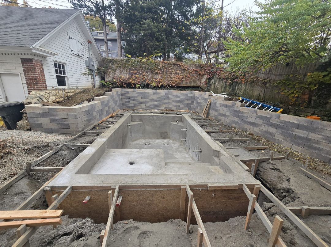 A large concrete pool is being built in the backyard of a house.