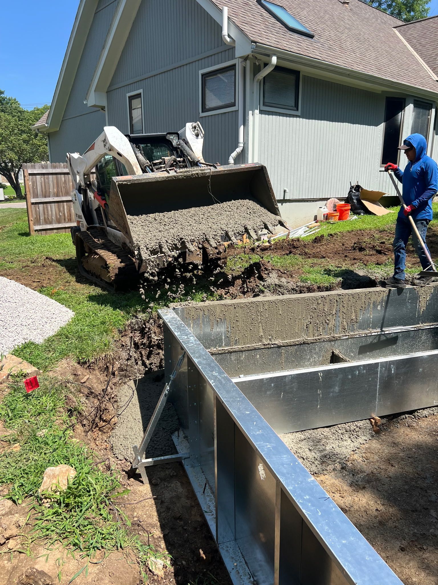 a Bobcat dumping concrete next to the steel pool walls