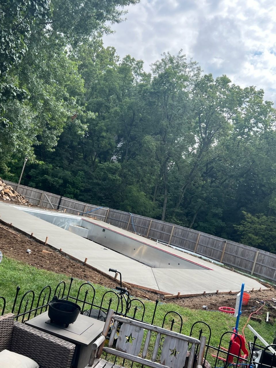 a rectangular pool under construction, surrounded by concrete and a wooded backdrop