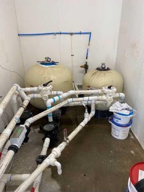 pool water filtration system with two large tanks, white PVC piping, valves, and a bucket