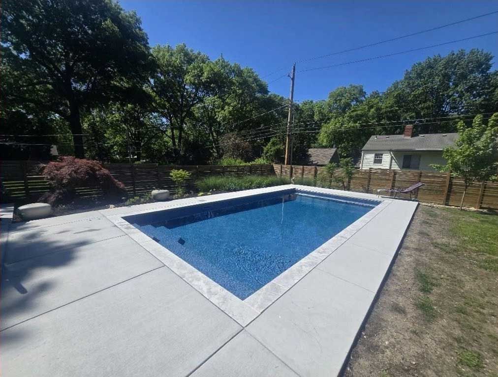 rectangular swimming pool with blue tile, concrete deck, and grassy backyard