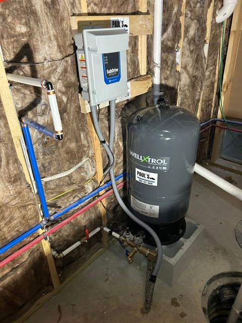 Water heater and plumbing system in an unfinished basement with exposed insulation and pipes.