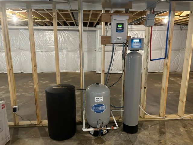 Basement utility room with water softener, black tank, and HVAC equipment against framed walls.