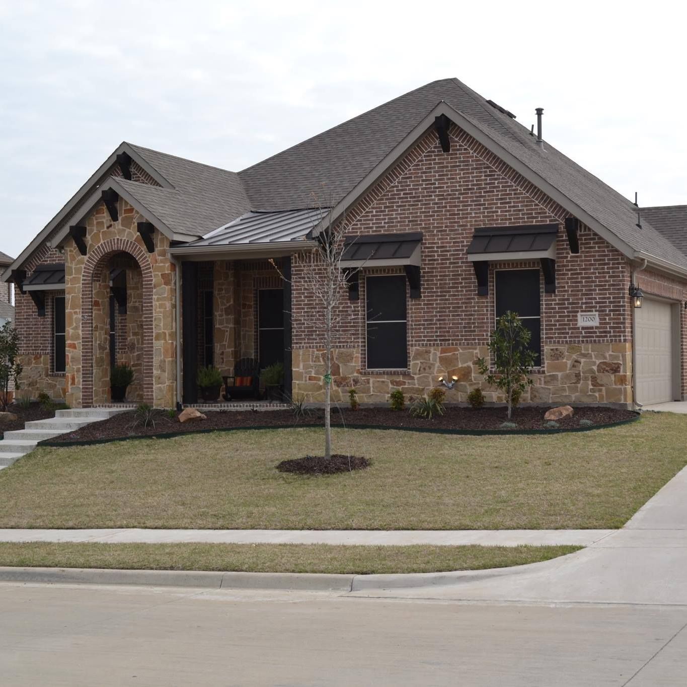 A brick house with a gray roof and a tree in front of it