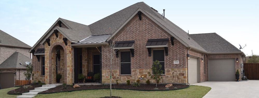 A large brick house with a gray roof is sitting on top of a lush green lawn.