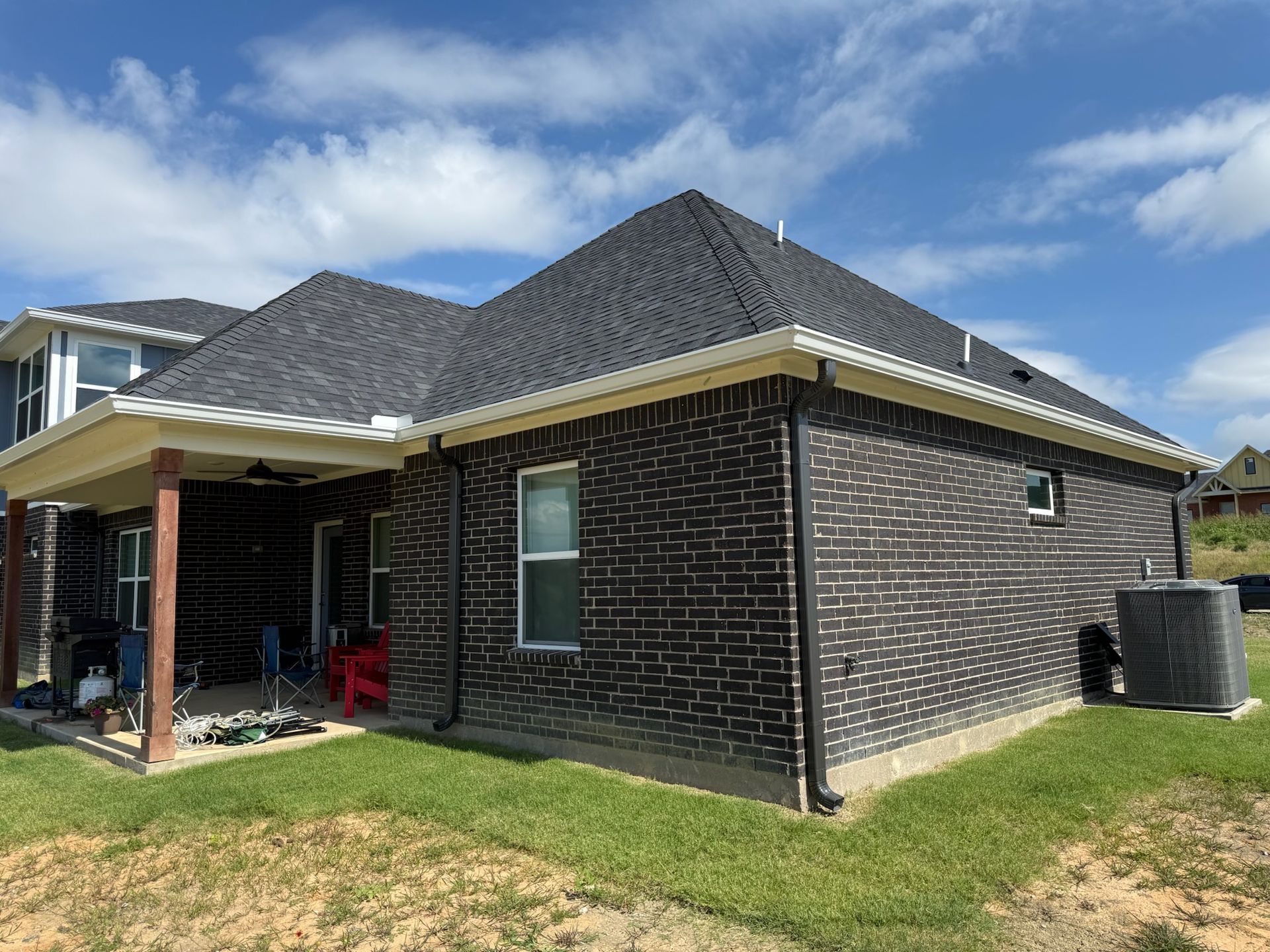 The back of a brick house with a covered porch and a black roof.