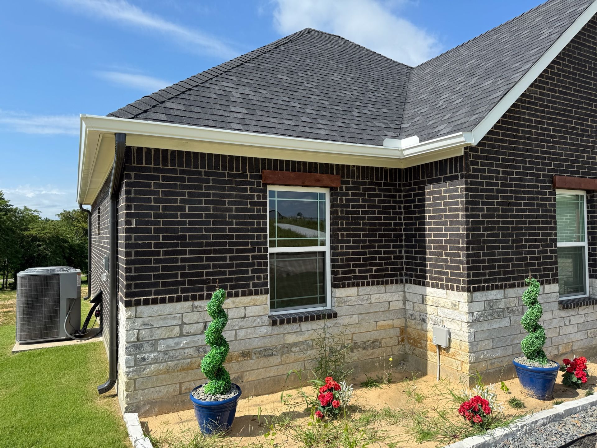 A brick house with a gray roof and potted plants in front of it.