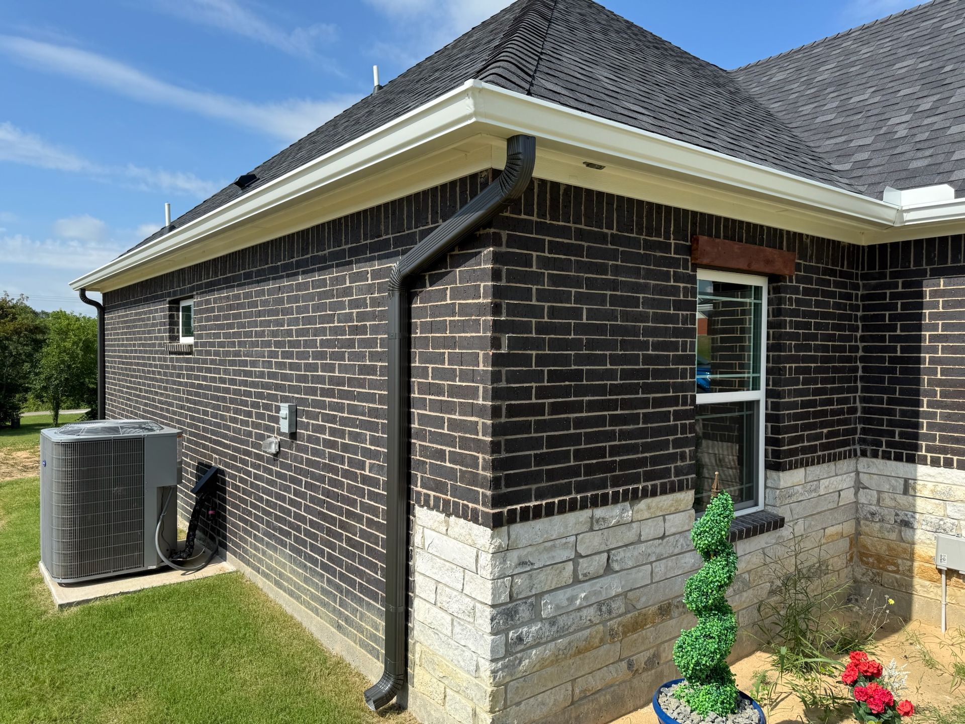 A black brick house with a black gutter and a window.