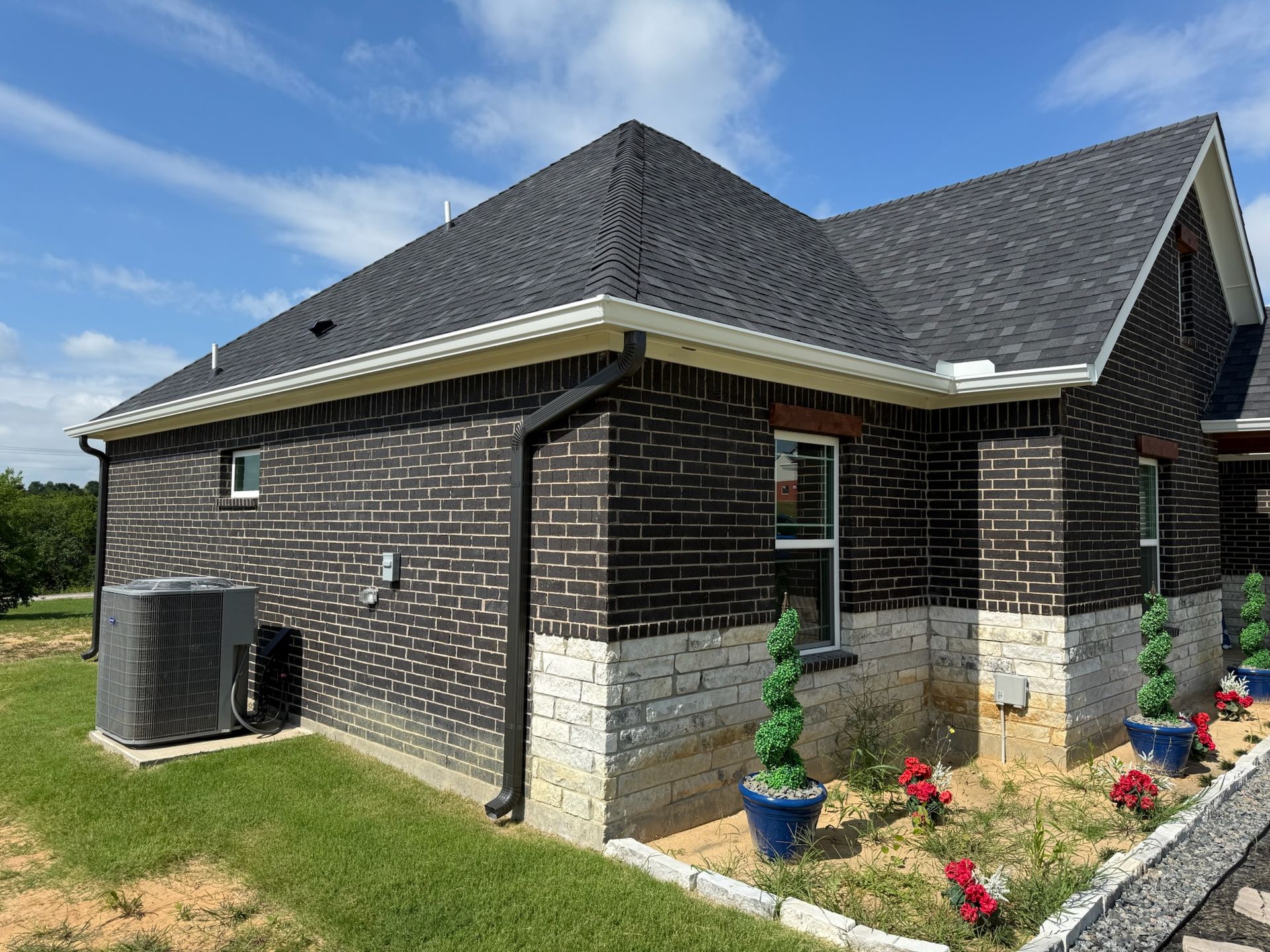 A brick house with a black roof is sitting on top of a lush green field.