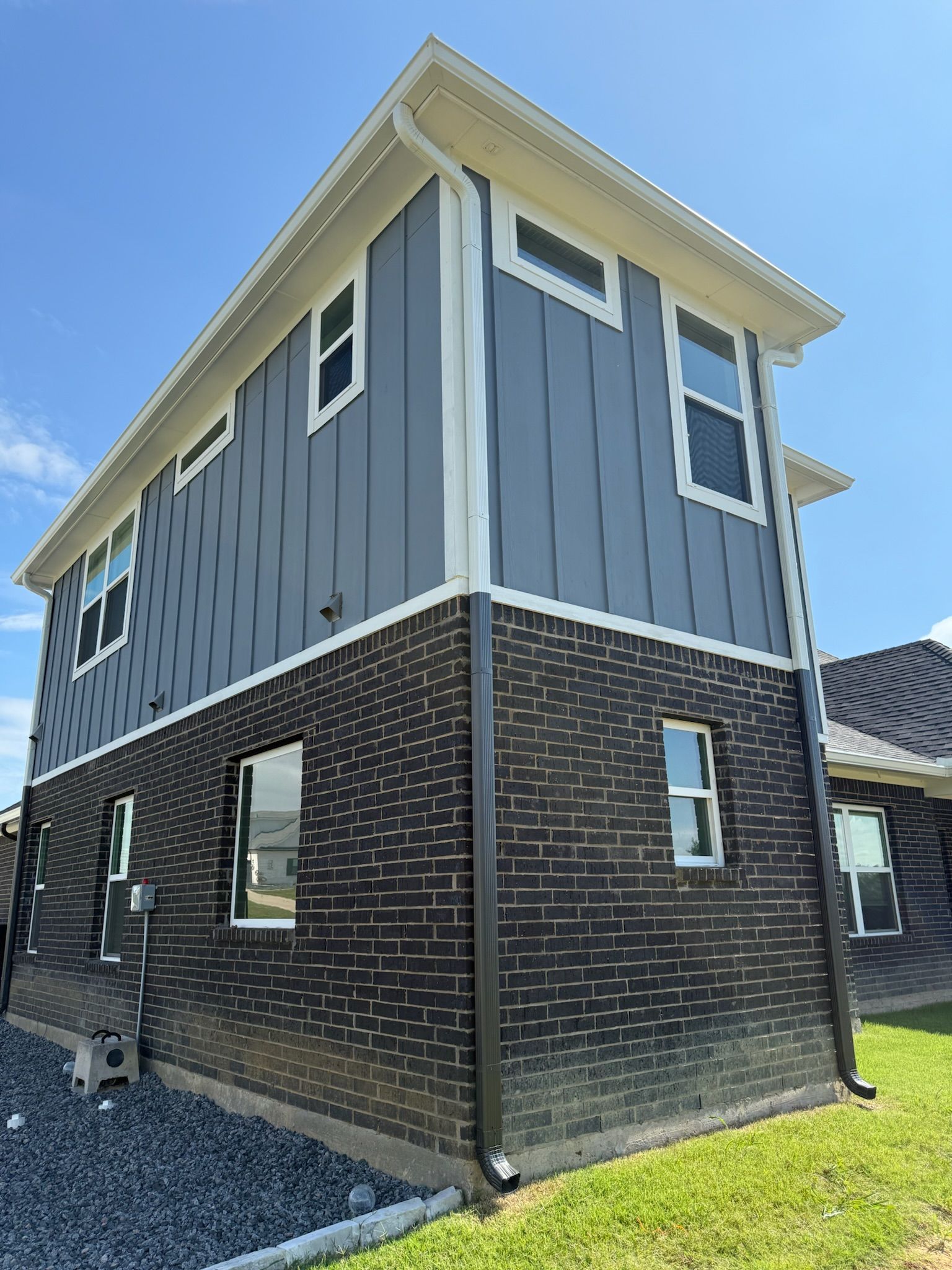 A large brick house with a gray siding and white trim is sitting on top of a lush green field.
