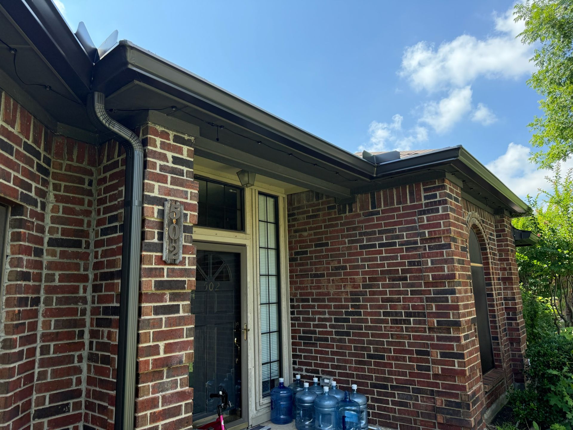 A brick house with a gutter and water bottles on the porch.