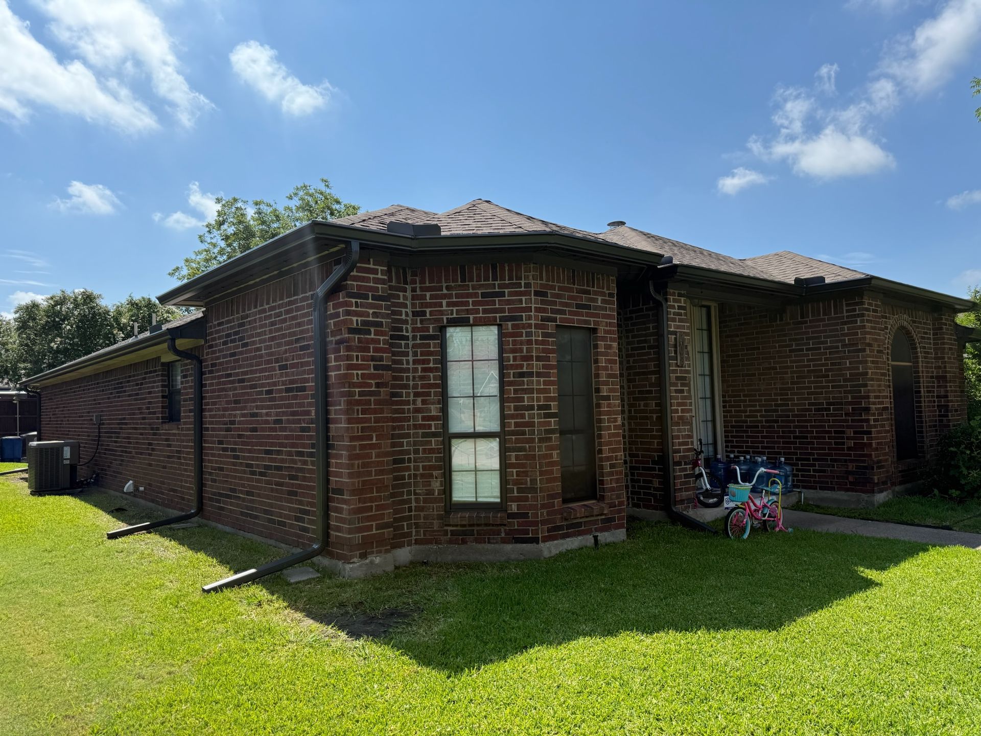A brick house with a bicycle in front of it on a sunny day.