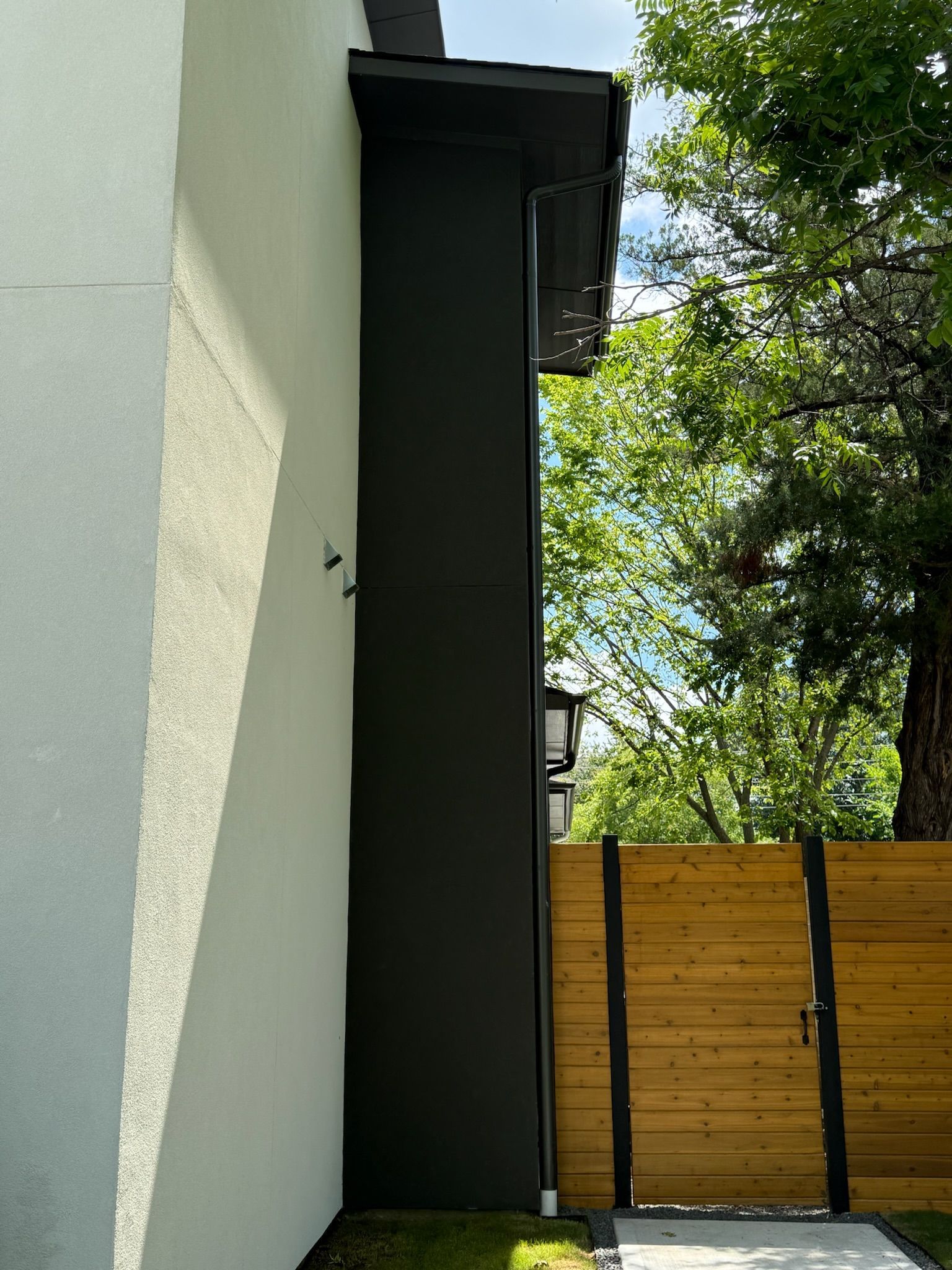 The side of a house with a wooden fence and a tree in the background.