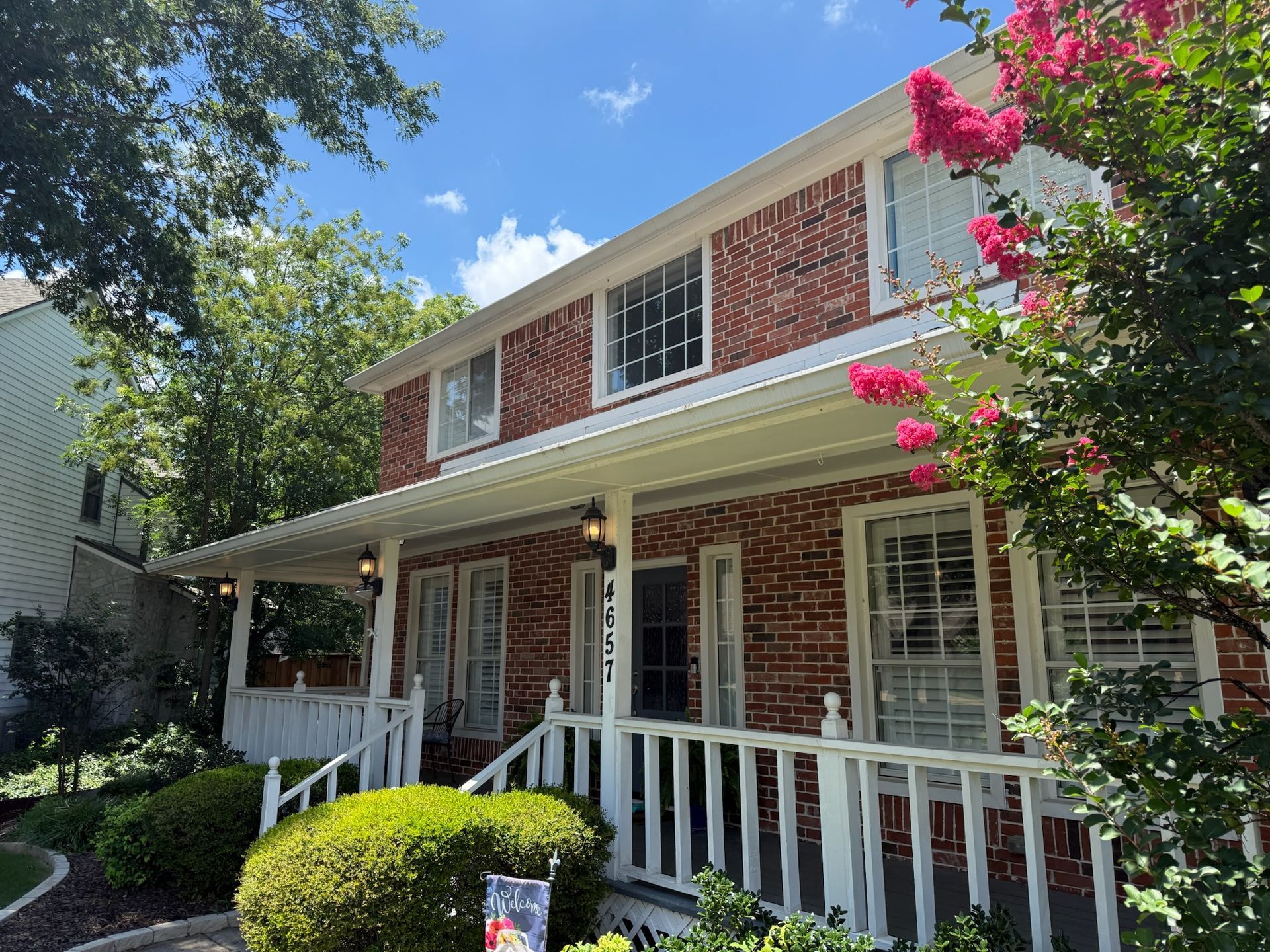 A brick house with a white porch and flowers in front of it.