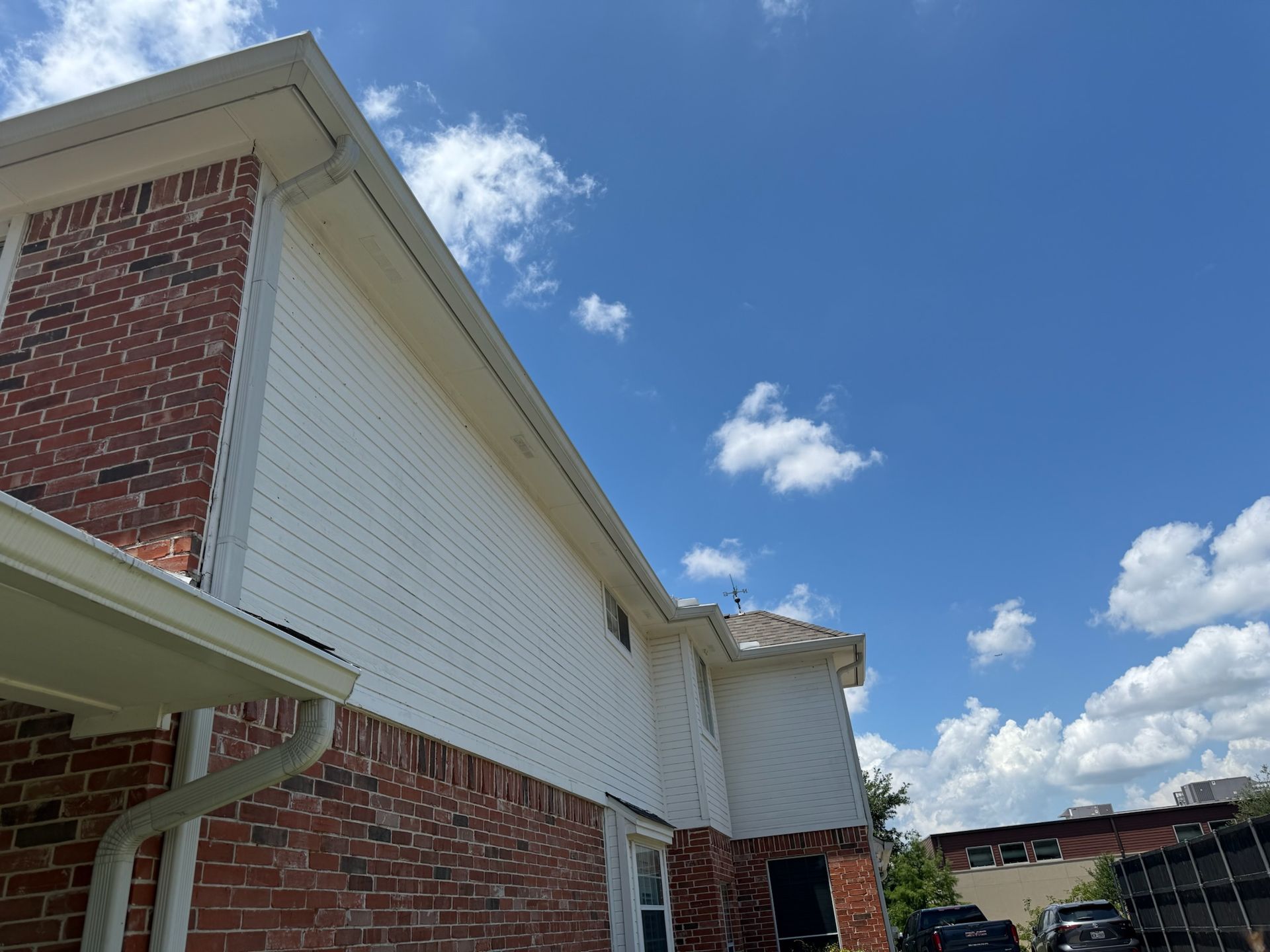 A brick house with a white siding and a white gutter on a sunny day.