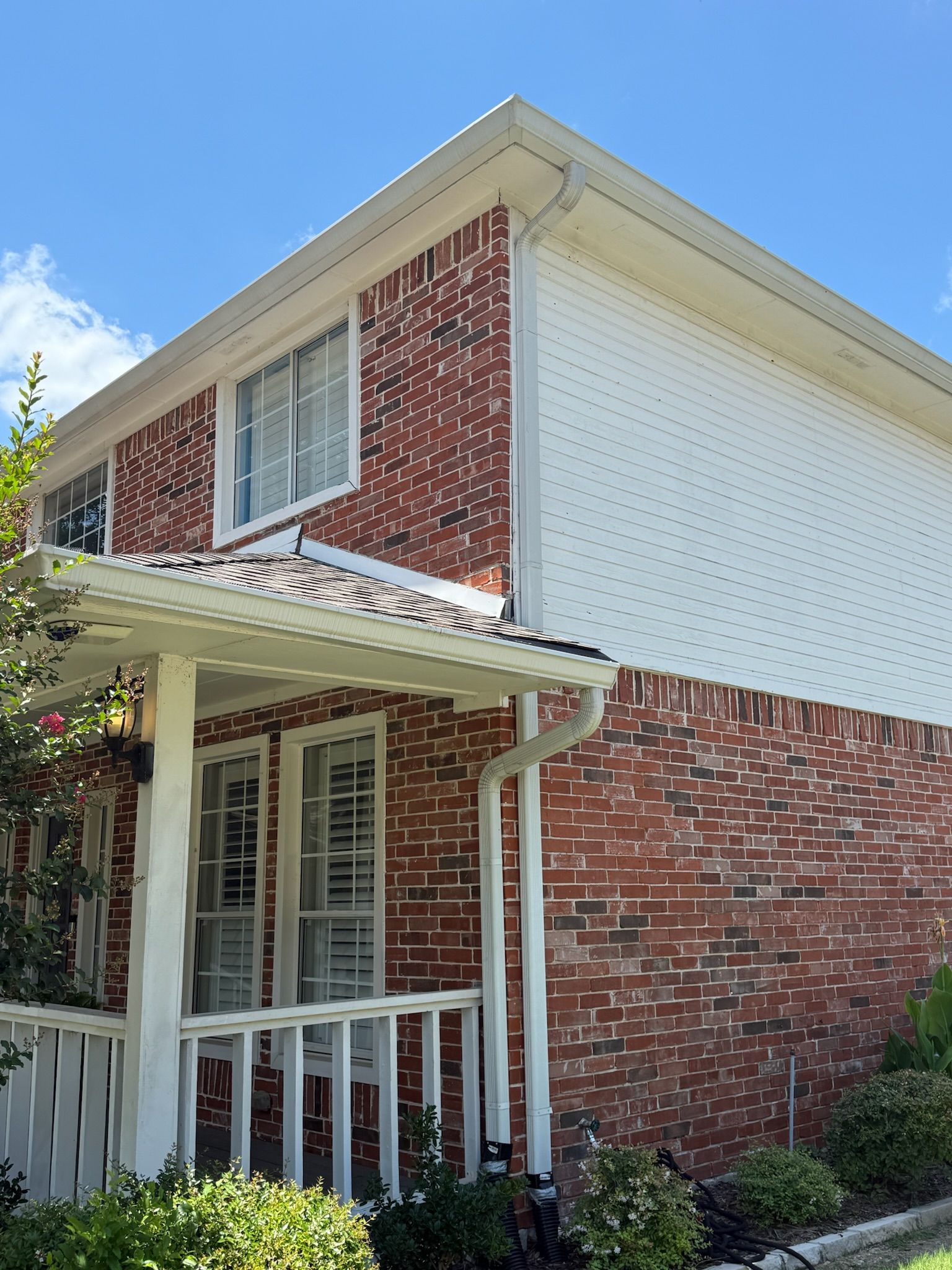 A red brick house with a white porch and a blue sky in the background.