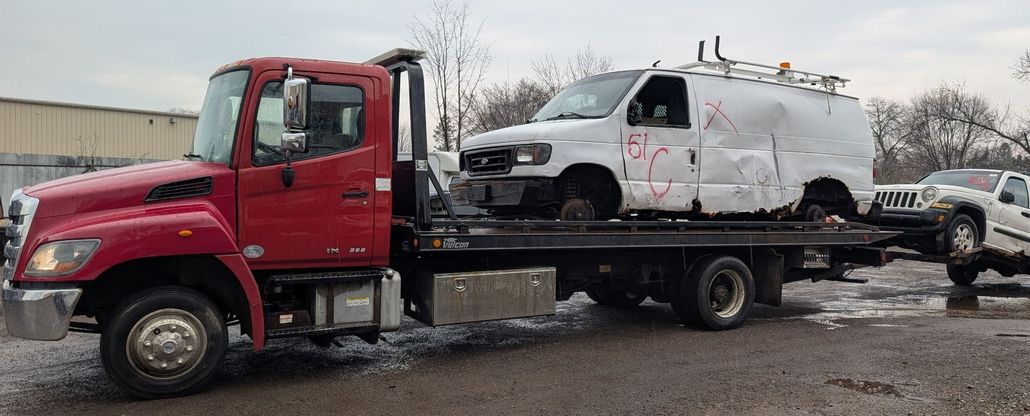 Red tow truck carrying a damaged white van and a light-colored pickup truck on a flatbed trailer.