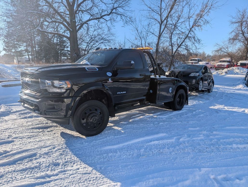 Black tow truck towing a car in a snowy, outdoor setting.