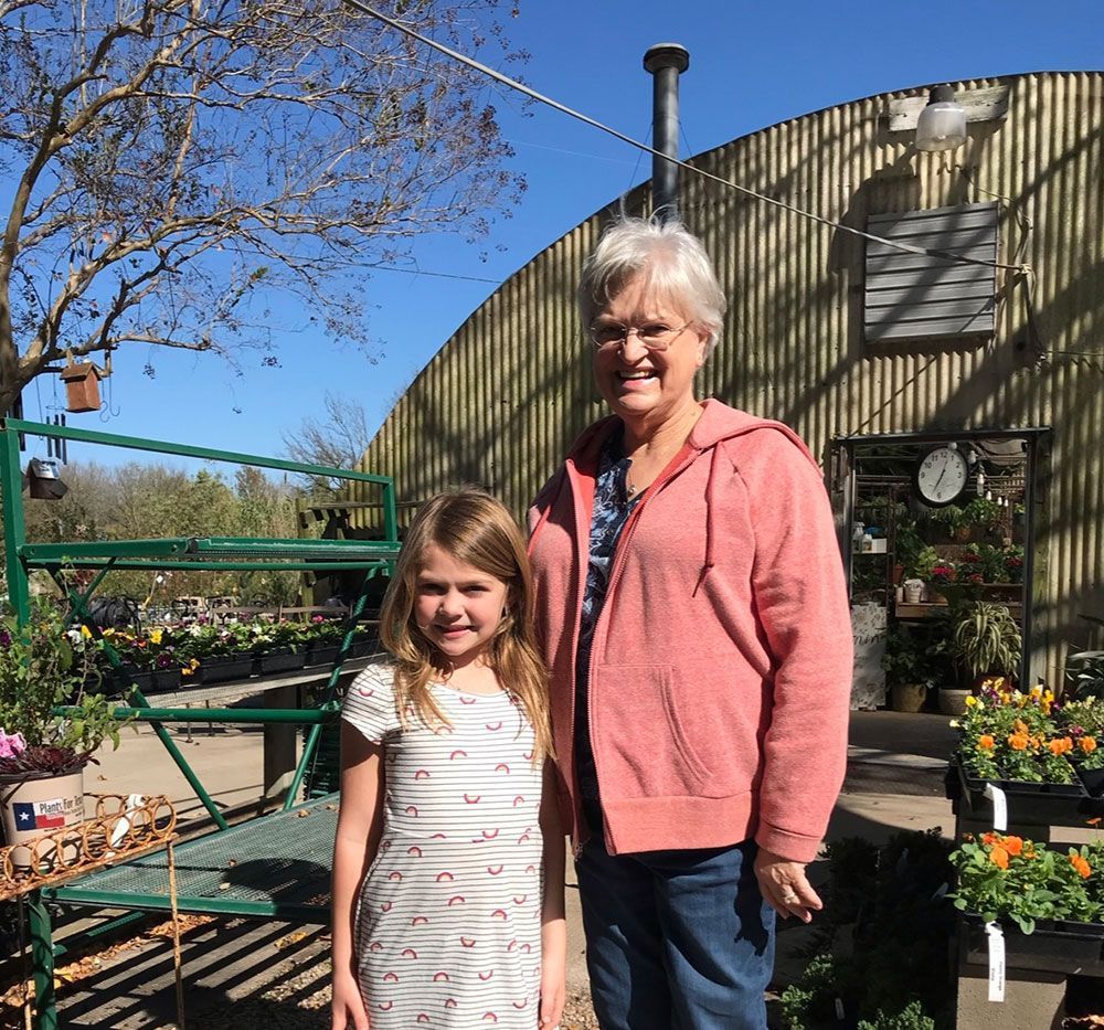 A woman and a little girl are standing in front of a greenhouse