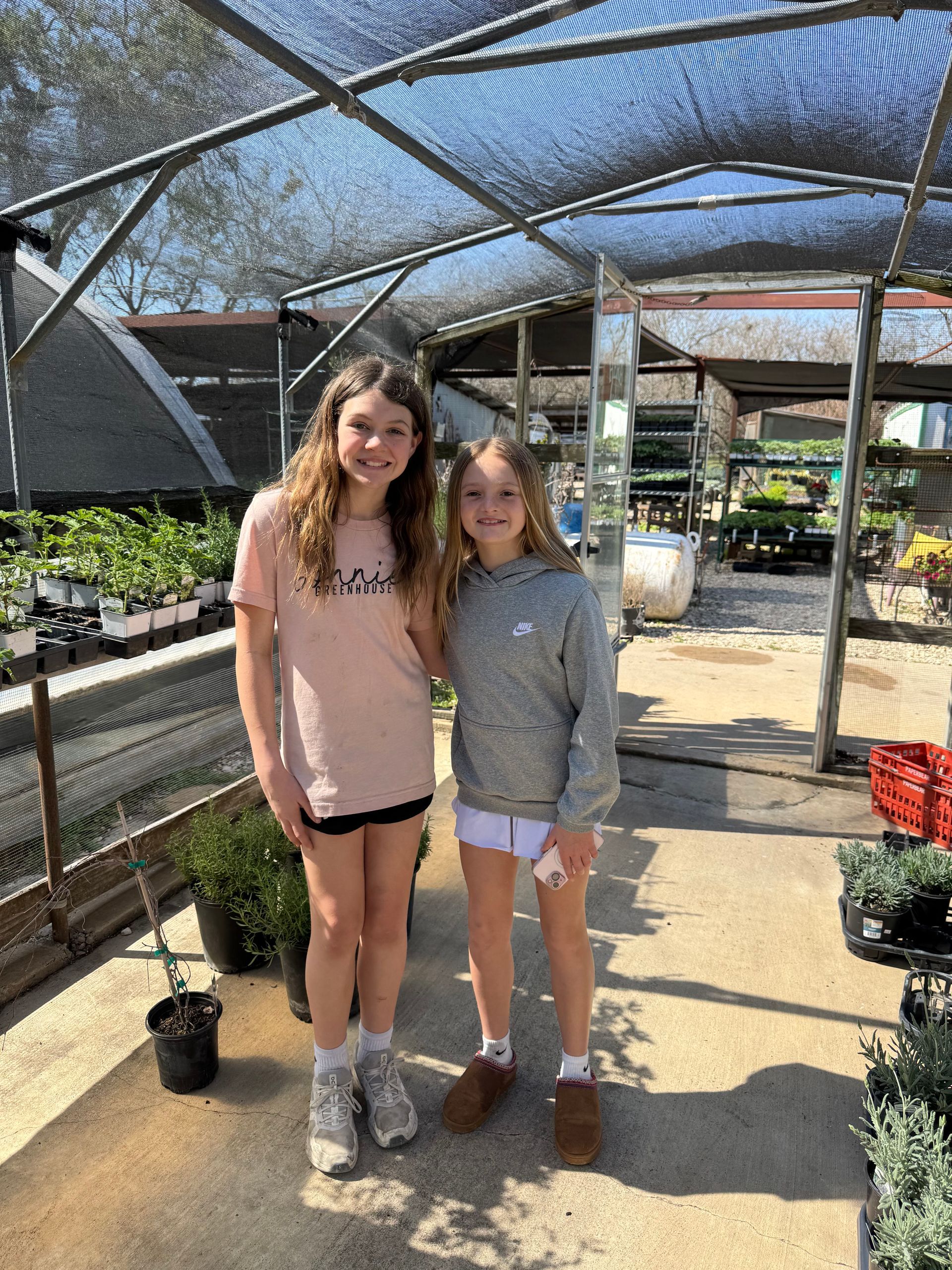 Two young girls are standing next to each other in a greenhouse.