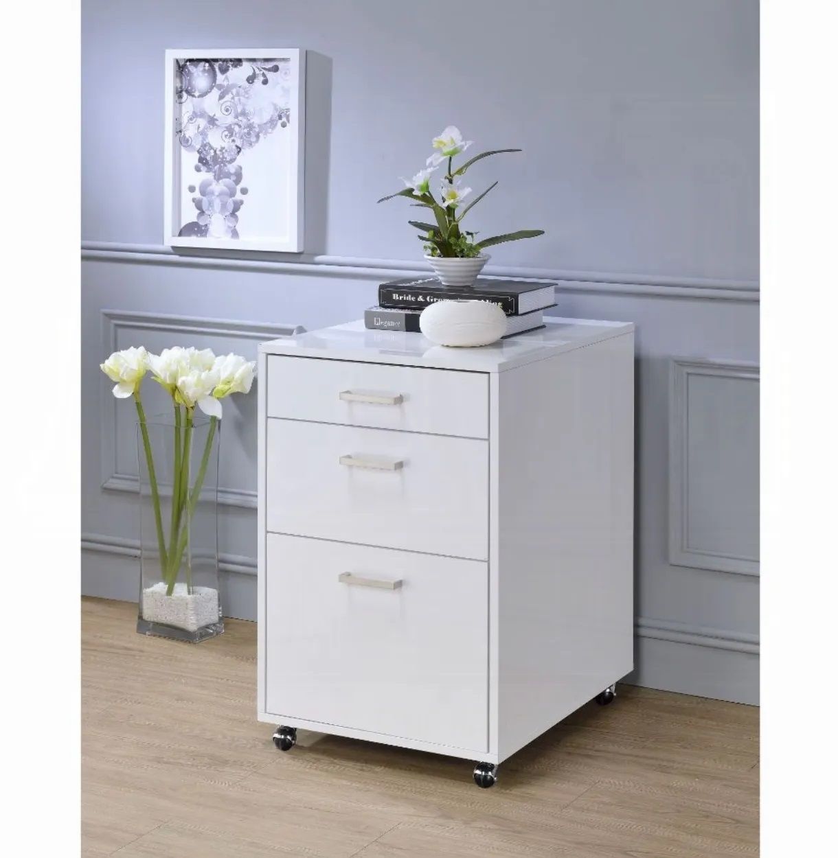 A white filing cabinet with three drawers and a vase of flowers on top.